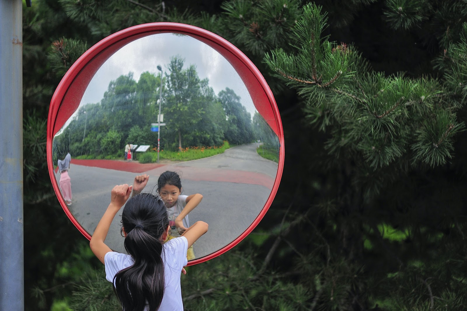 A convex mirror, used in road, bends,  which is used to prevent accident. A child is seeing her reflection in the convex mirror placed along the road side